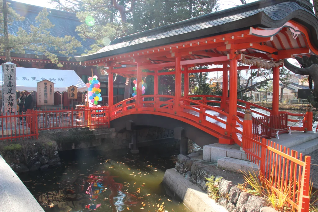 秋の陽光に照らされる生島足島神社の朱塗りの屋根付き御神橋