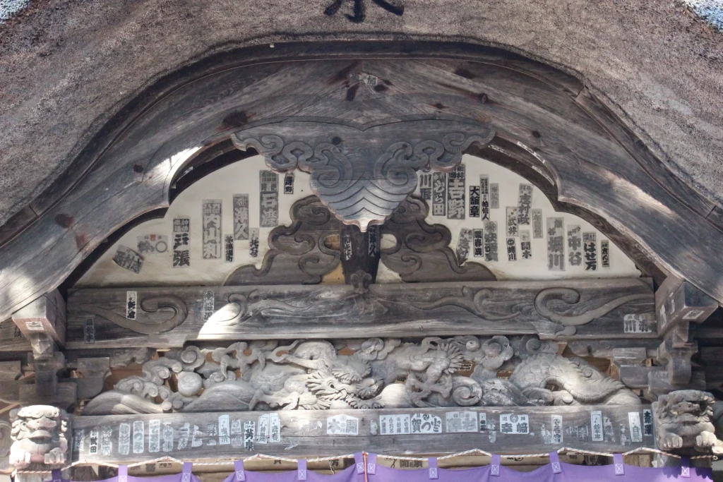龍などの精巧な木彫細工と千社札が貼られた前山寺本堂向拝のアップ