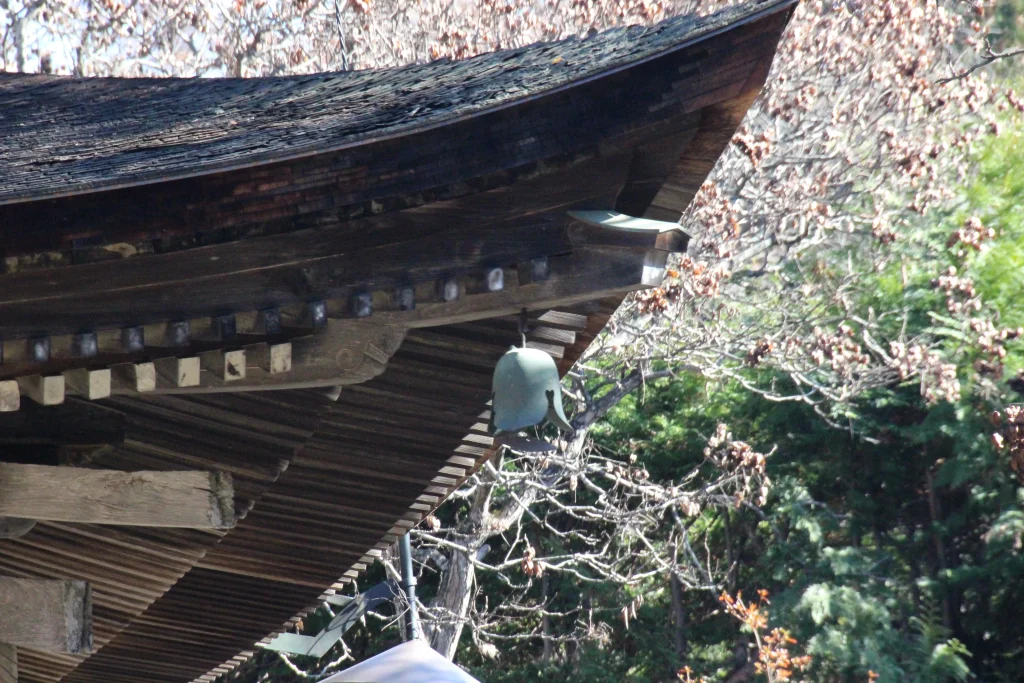 三重塔の屋根の角から吊るされた真鍮製の風鐸（ふうたく）のアップ