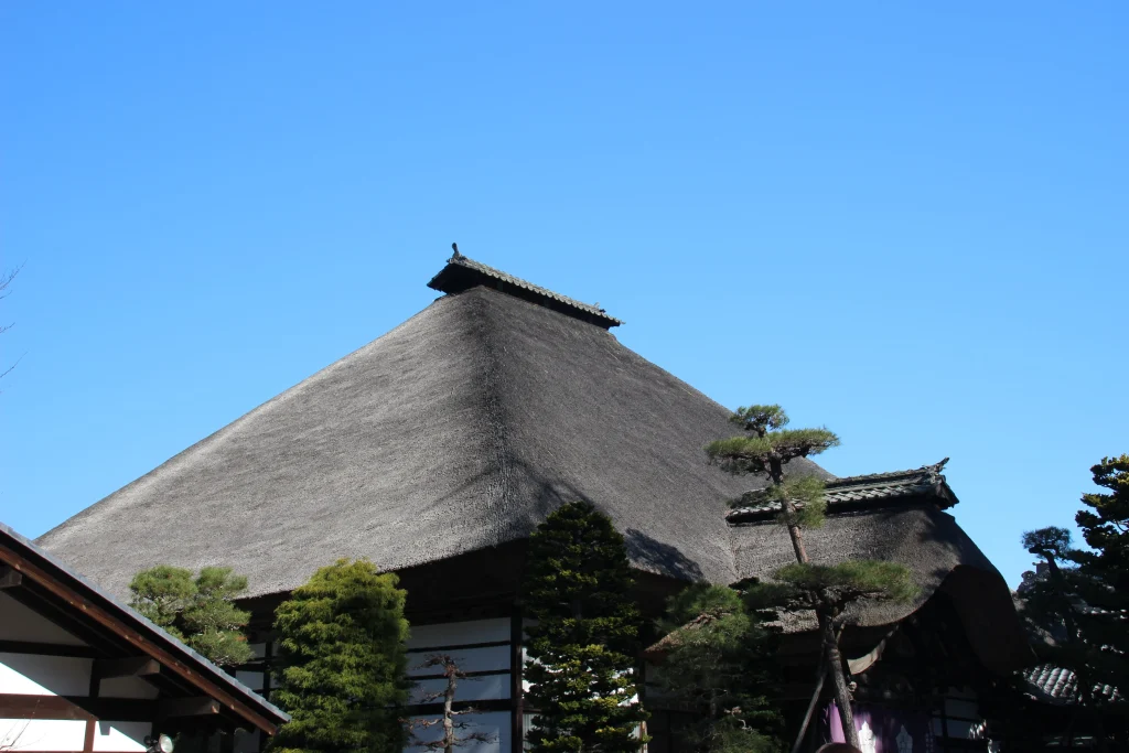 美しい寄棟造りの茅葺き屋根と青空が織りなす本堂上部のカット