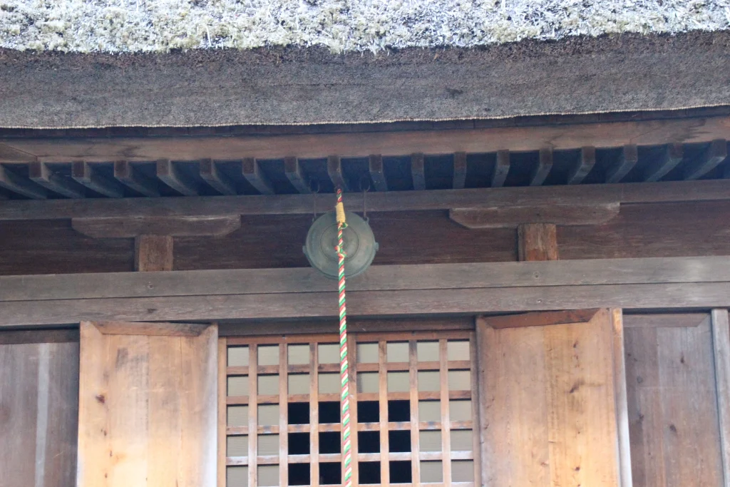 中禅寺薬師堂の正面入口に掲げられた古びた青銅製の鰐口と下げ紐