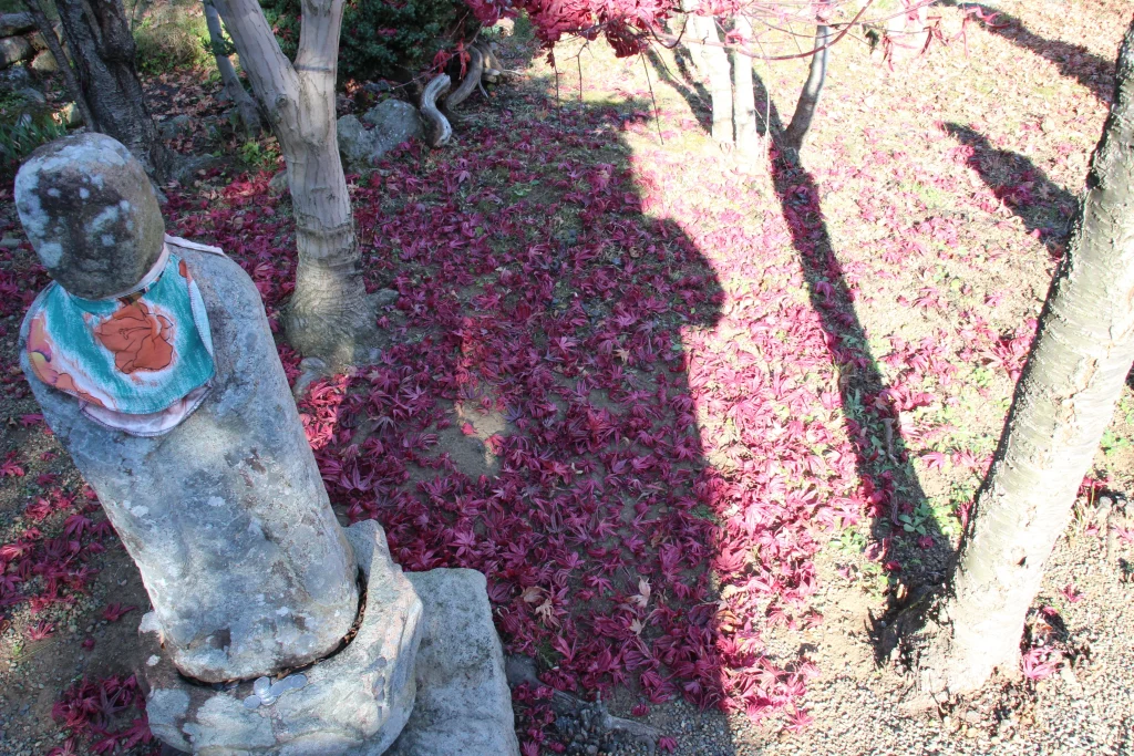 紅葉したもみじの散り葉が敷き詰められた地面と佇む小さな石仏(お地蔵様)