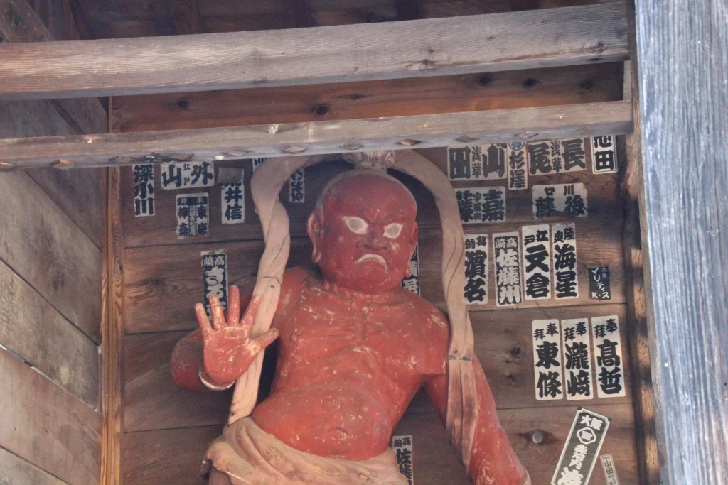 歴史を感じさせる多数の千社札が貼られた中禅寺仁王門の木壁と格子戸の奥の吽形像