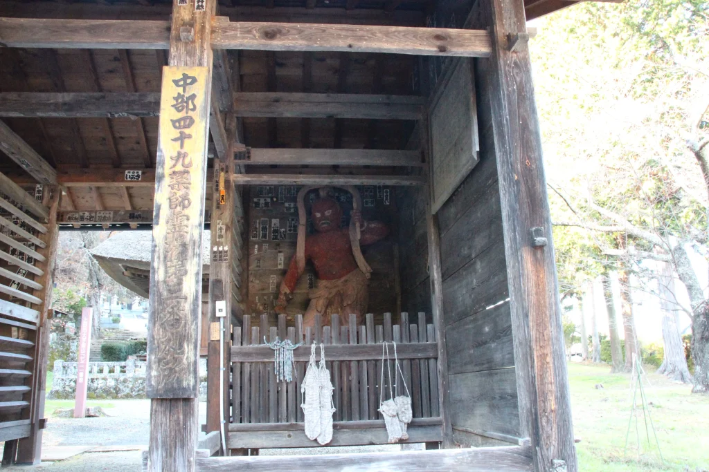 仁王門の格子戸越しに静かに佇む中禅寺の赤い木造金剛力士立像(吽形像)