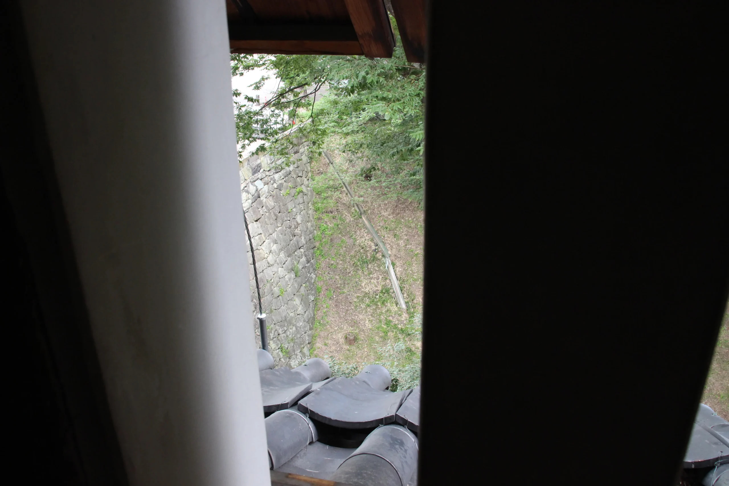 南櫓の武者窓から下を見下ろした本瓦葺きの屋根と険しい石垣の景色