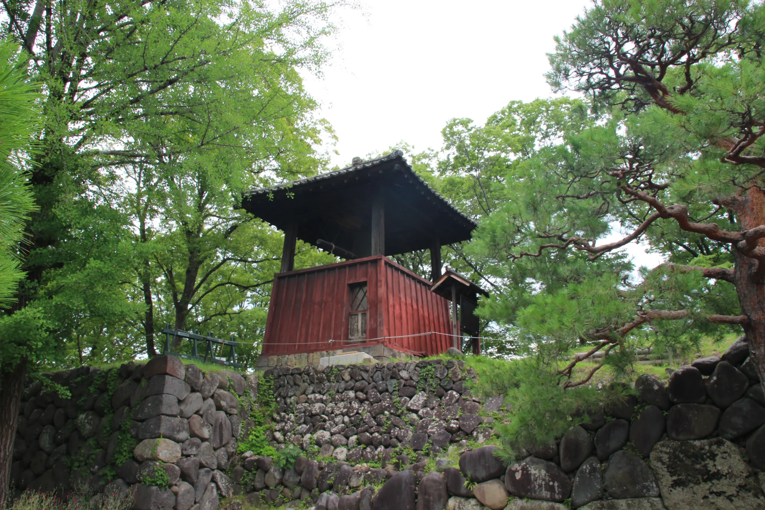 上田城跡公園に建つ朱塗りの板壁が美しい「平和の鐘」の鐘楼と周囲の木々
