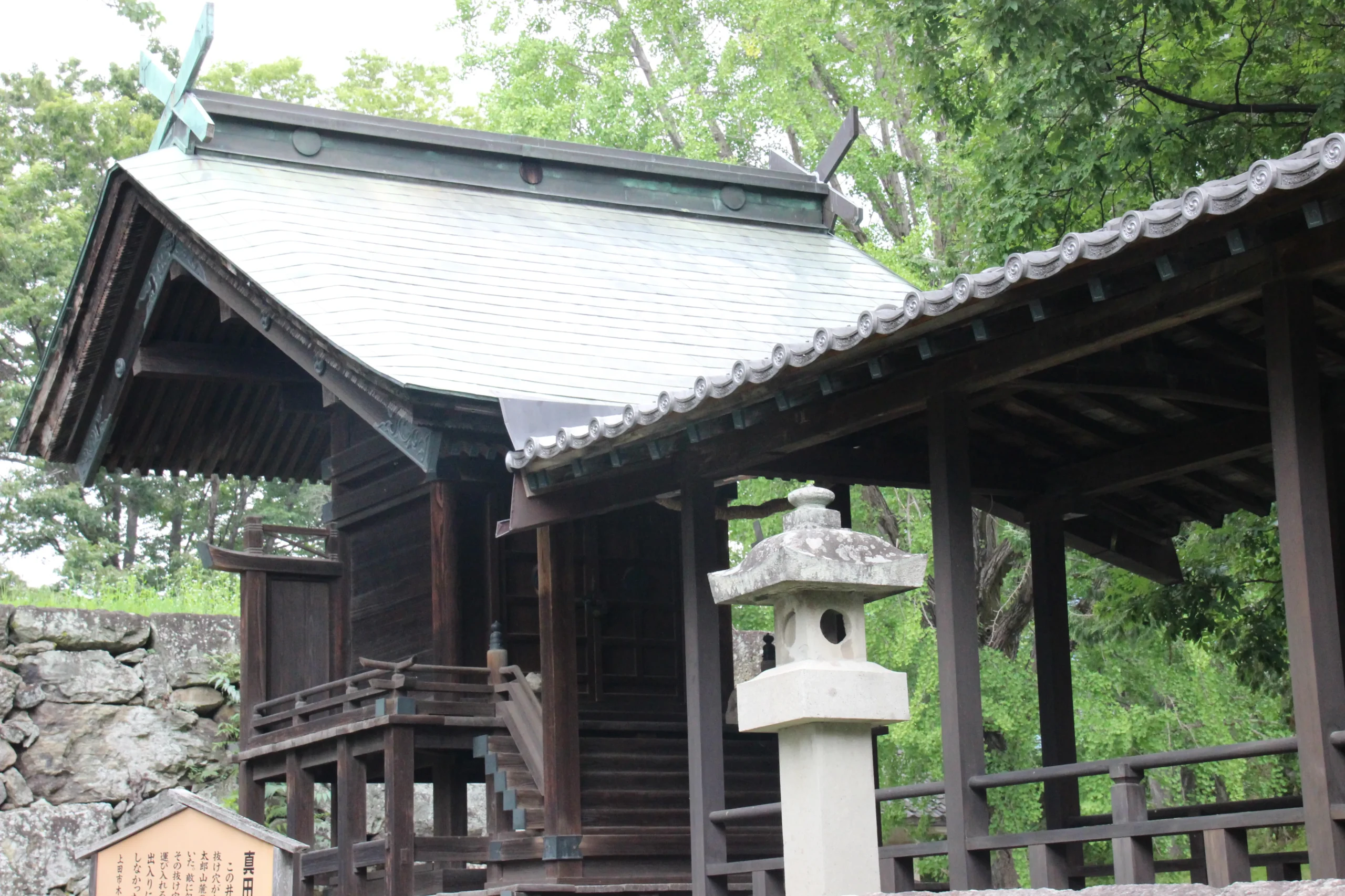 眞田神社の本殿脇にひっそりと佇む木造の末社と素朴な石灯籠