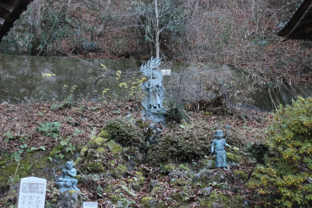 不動堂の脇の斜面に祀られた青銅の不動明王立像と周囲の童子像
