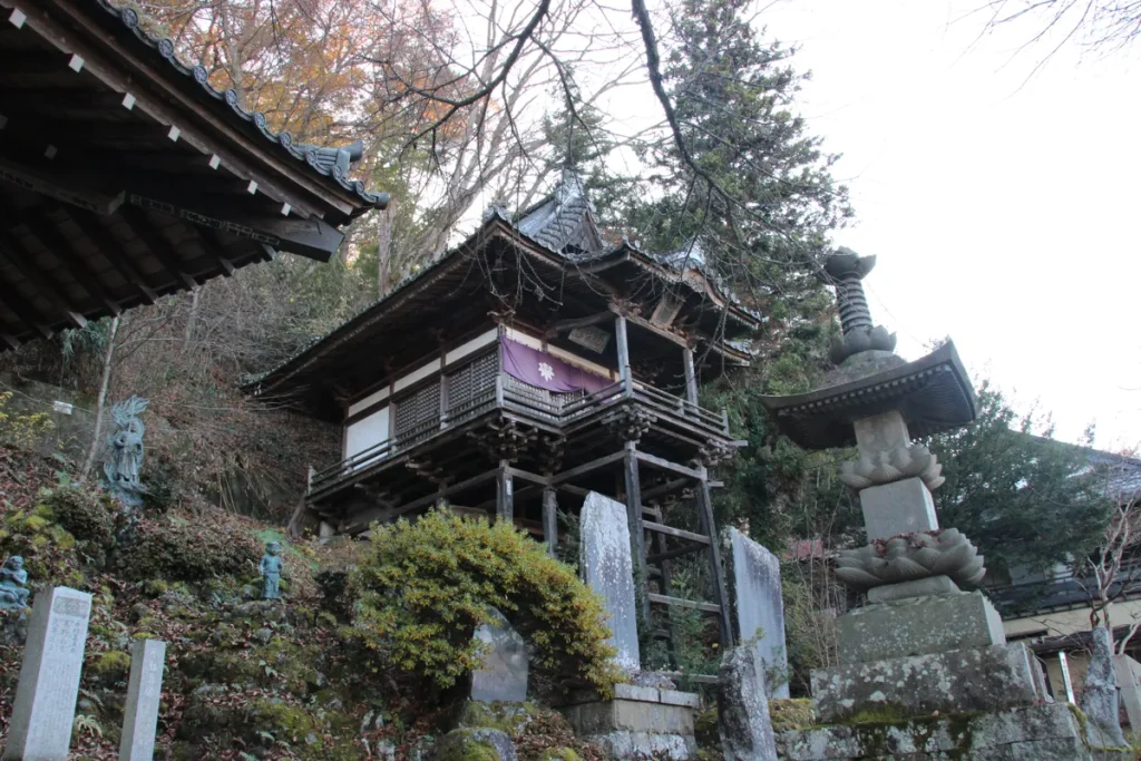 舞台造りの薬師堂と手前に建つ苔むした歴史ある石造宝篋印塔