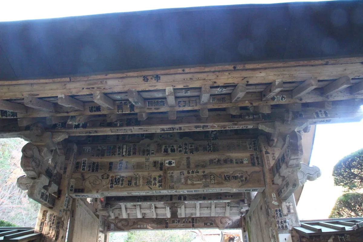 多くの千社札が貼られた安楽寺山門の緻密な組物・木組みの様子