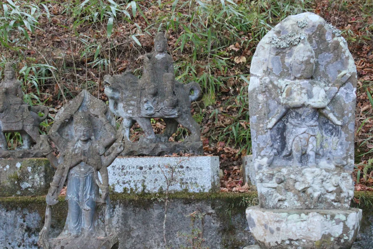 並んで祀られた「馬頭観音」などの文字や像が彫られた苔むした石仏のアップ