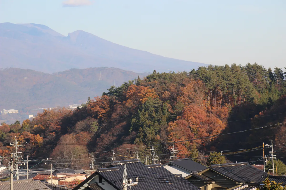別所温泉街の屋根越しに望む美しく化粧した秋の里山と遠くの山々の遠景