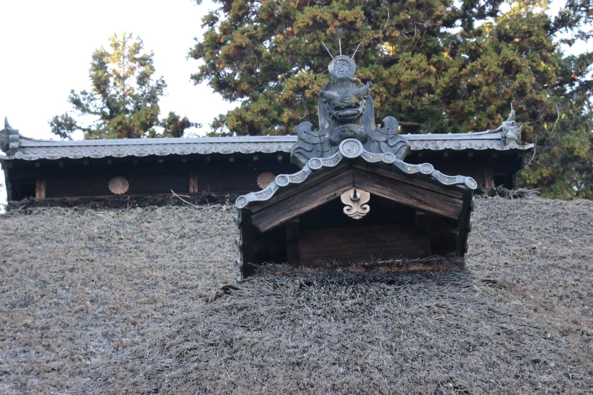 茅葺き屋根の中央に設けられた特徴的な煙出しの窓構造と飾られた鬼瓦のアップ