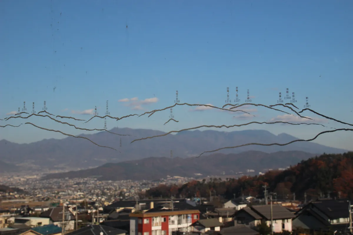 アクリル案内板に描かれた山の稜線の彫刻線と、背景にある実際の山並みがきれいに重なる様子