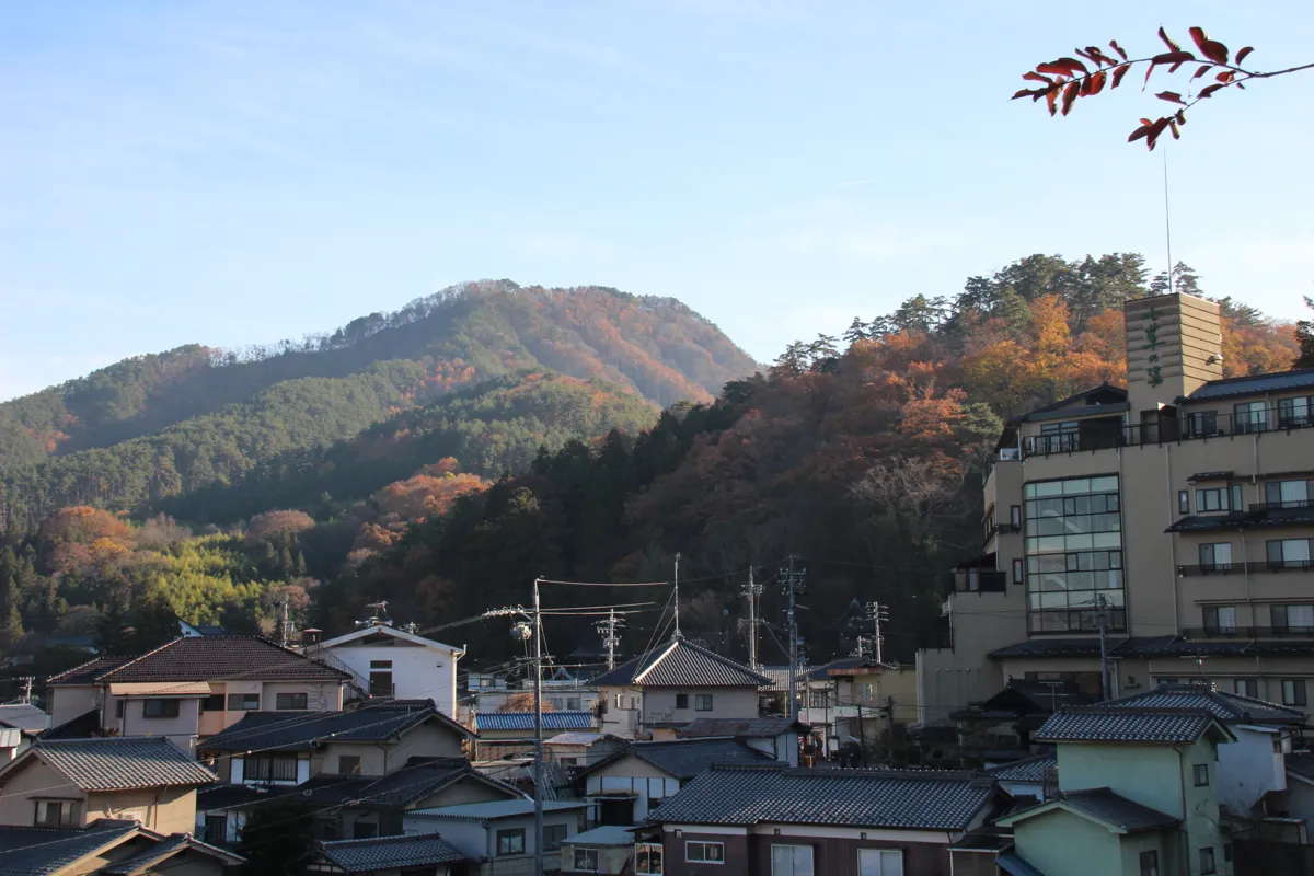 別所温泉街の近代的な旅館の建物と、その背後に広がる秋の美しい紅葉に染まる山