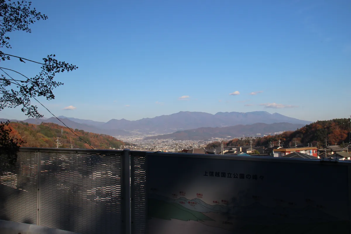 展望台の手すりと山名案内看板、その背景に広がる広大な塩田平と美しい山並みの全景