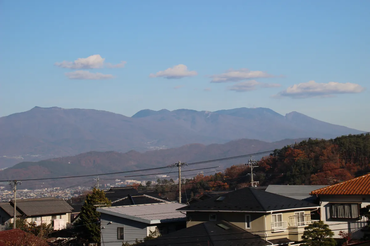 別所温泉の民家の屋根越しに広がる、青空と信州上田の豊かな山々の稜線