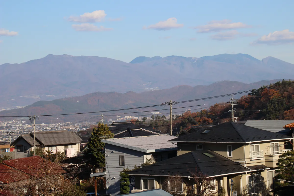 別所温泉の民家と電柱の向こうに広がる、澄んだ青空と信州山岳の景観