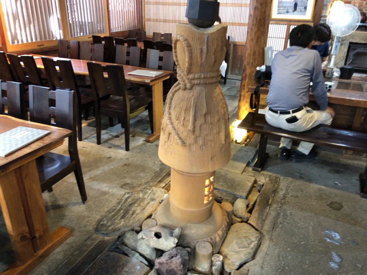 そば処おおにしの店内中央に設置された、しめ縄と藁で包まれた古めかしい石碑（道祖神）と石畳の囲炉裏