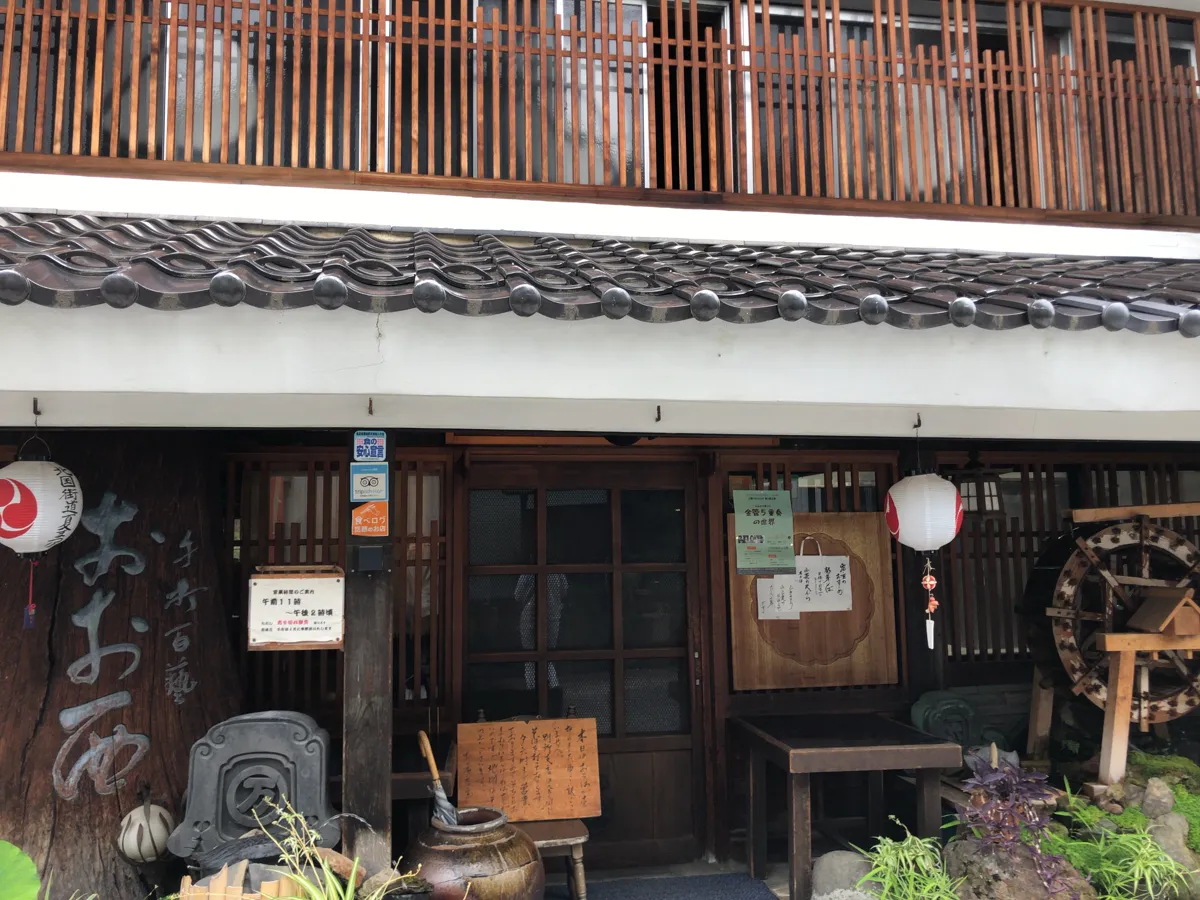 店舗の前に設置された趣のある水車と、風に揺れる「おおにし」の看板や格子の店舗入口のアップ