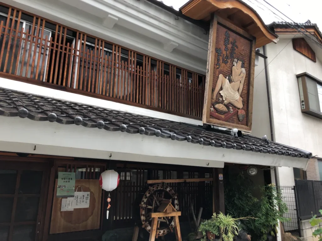 そばを打つ名人の姿が生き生きと彫られた特徴的な木製看板と「十割百藝 おおにし」の風情豊かな白壁の店舗外観