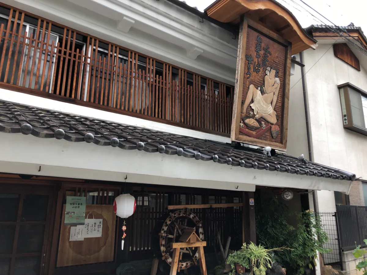 そばを打つ名人の姿が生き生きと彫られた特徴的な木製看板と「十割百藝 おおにし」の風情豊かな白壁の店舗外観