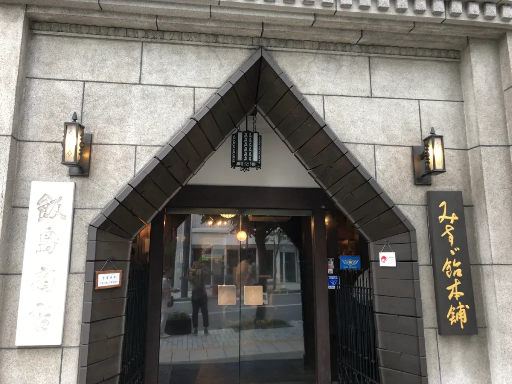 飯島商店の正面玄関にあるみすず飴本舗と金文字で書かれた重厚な木製看板と三角形の石造りアーチの入り口