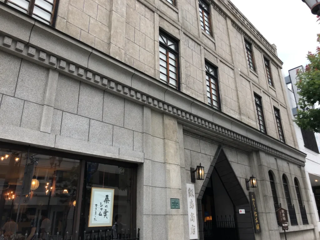 桑の実ジャムできましたという手書きの案内が貼られた飯島商店のショーウィンドウと重厚な石造りの店舗外観